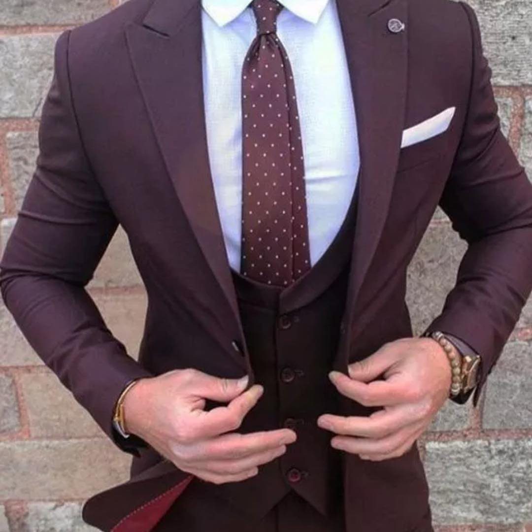 A man wearing a tailored burgundy three-piece suit with a white shirt and polka-dot tie.