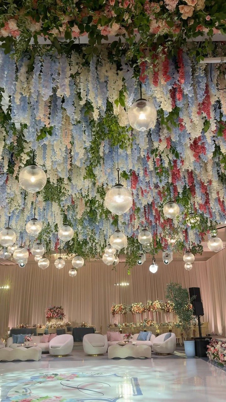 Hanging blue and pink wisteria flowers with glass globe lights decorating a wedding ballroom reception space.
