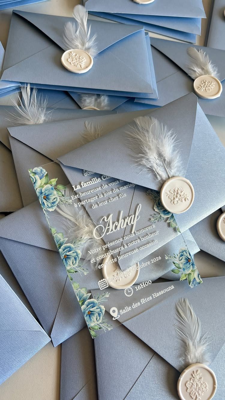 Clear acrylic wedding invitations with blue floral designs and dusty blue envelopes with white wax seals.