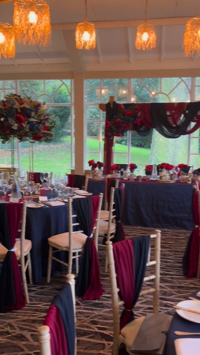 Wedding tables set with navy blue linens and burgundy fabric chair sashes under warm lights.
