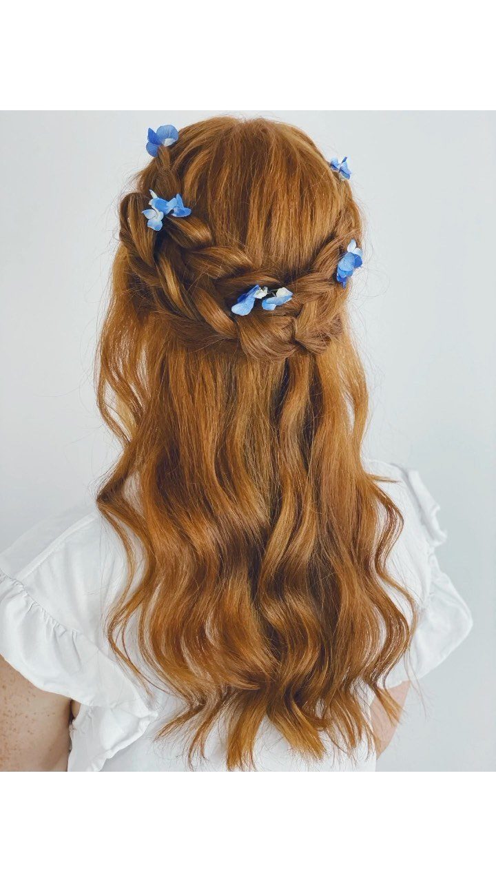 Long wavy red hair styled in a half-up braid decorated with small blue flowers.