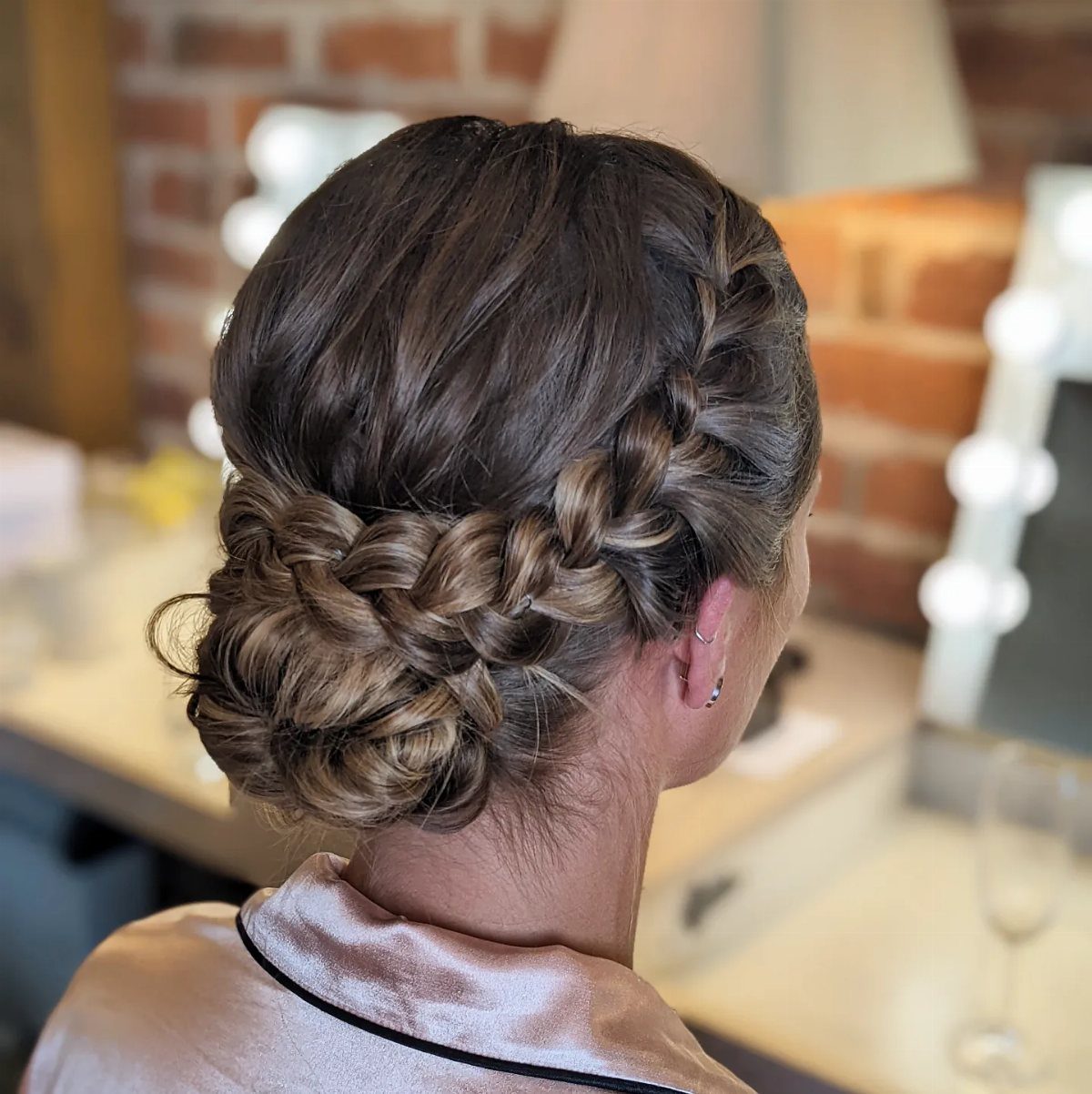 Woman with light brown hair styled in a thick side braid and a low textured bun.
