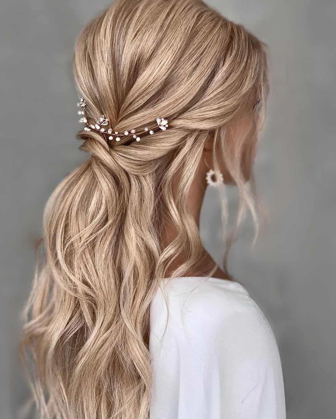 Long blonde wavy hair styled in a half-updo with a pearl hair vine accessory.