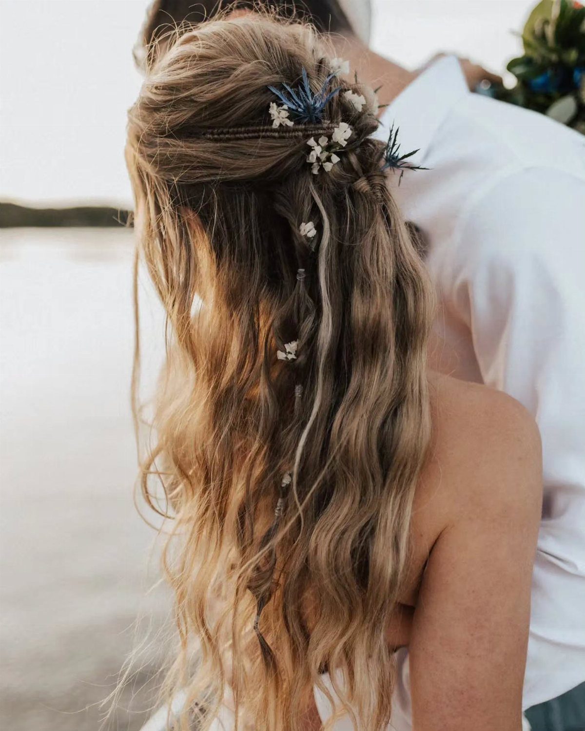 Long blonde wavy hair with small braids and tiny white dried flowers in a half-updo style.