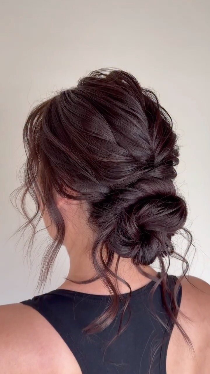 Dark brown hair styled in a textured messy low bun with loose wavy tendrils.