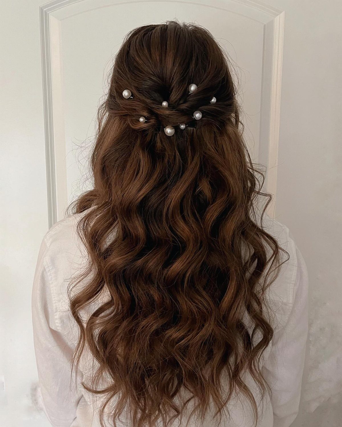 Long wavy brunette hair styled in a half-updo with small white pearl hair pins.