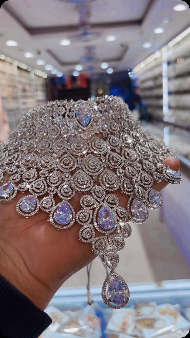 11 Bridal Diamond Necklace Ideas for Your Ceremony 7 A hand holding a large, intricate silver diamond necklace with iridescent teardrop pendants.
