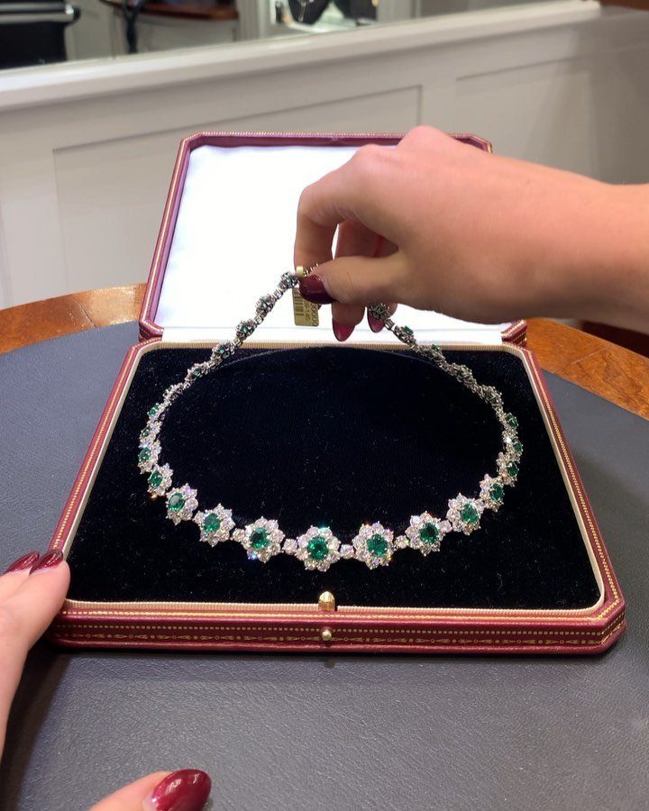 11 Bridal Diamond Necklace Ideas for Your Ceremony 4 Hands holding an open jewelry box displaying a diamond and emerald necklace.