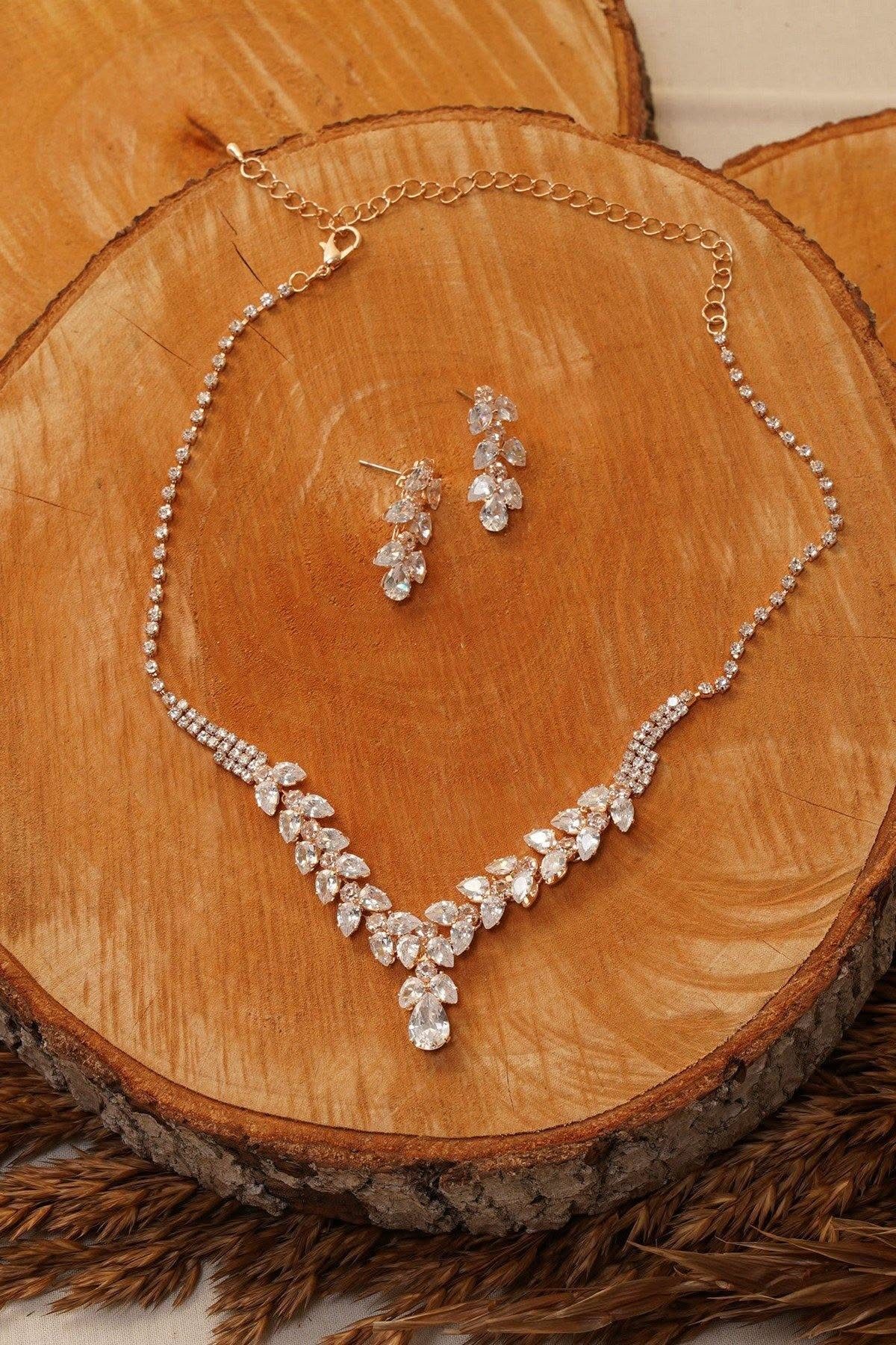 11 Bridal Diamond Necklace Ideas for Your Ceremony 1 Gold-toned diamond necklace and matching earrings resting on a rustic wooden slice.