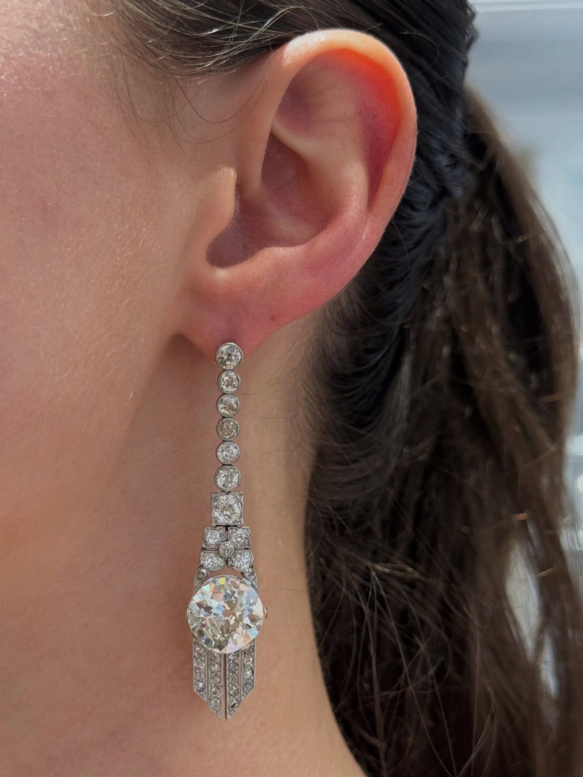 A long Art Deco style diamond drop earring hanging from a person's earlobe.