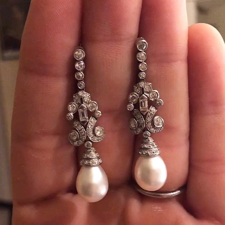 Art Deco style silver drop earrings with clear stones and large white pearl pendants held in a hand.