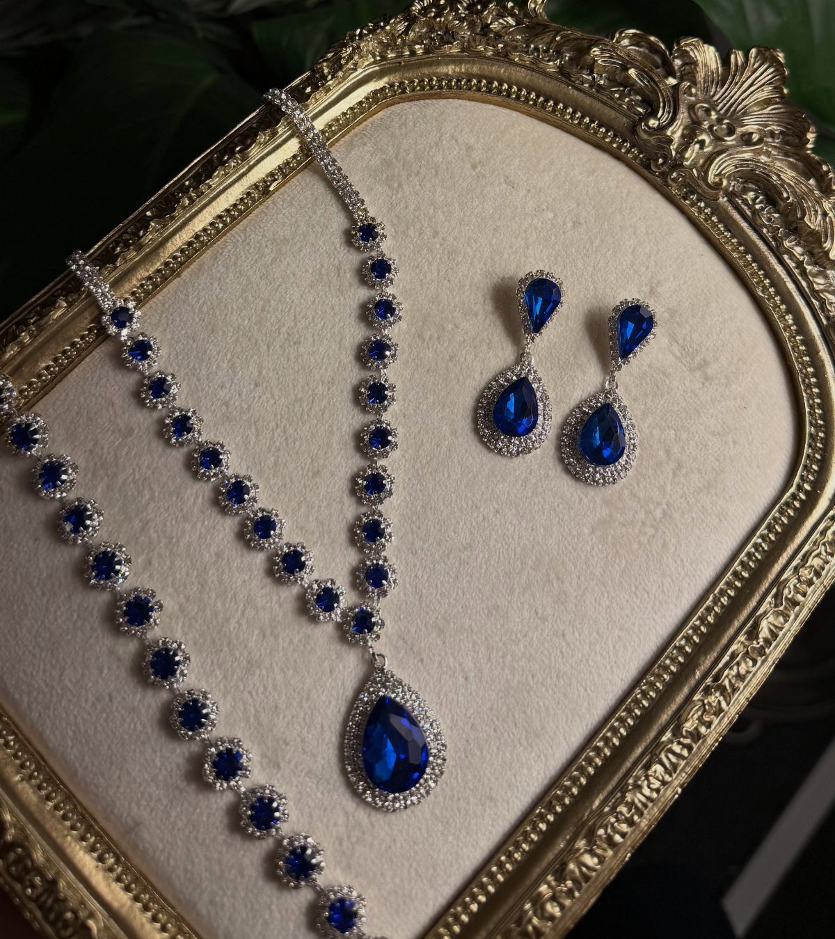 Blue teardrop gemstone necklace and matching earrings set inside a gold ornate frame.