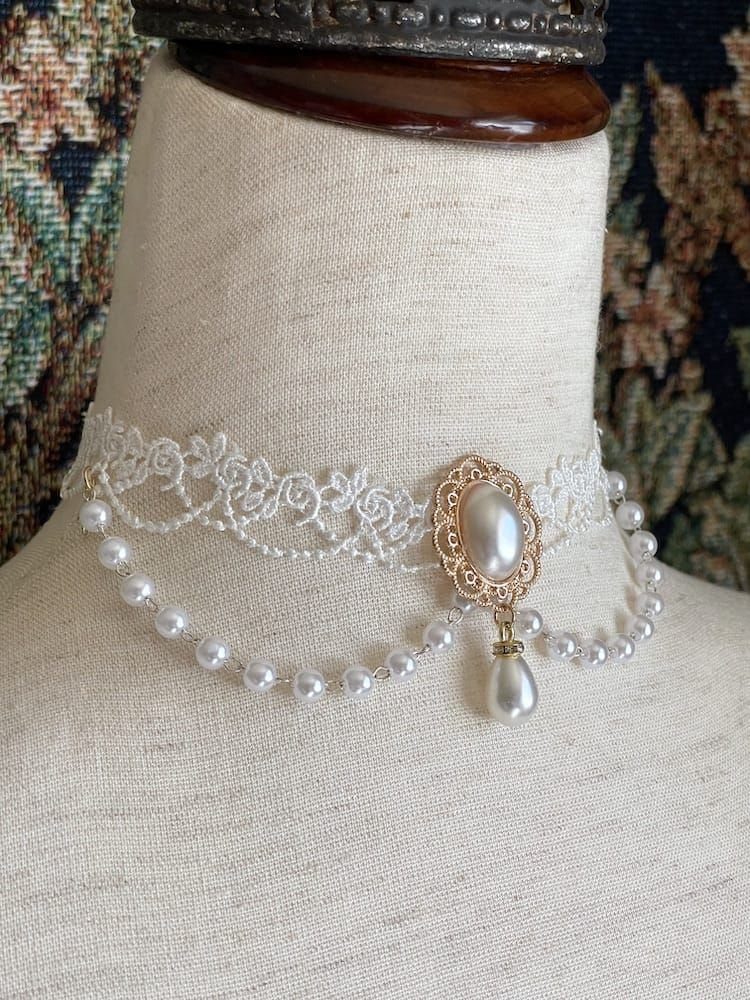 A dual-strand lace and pearl choker necklace with a gold medallion and pearl drop.