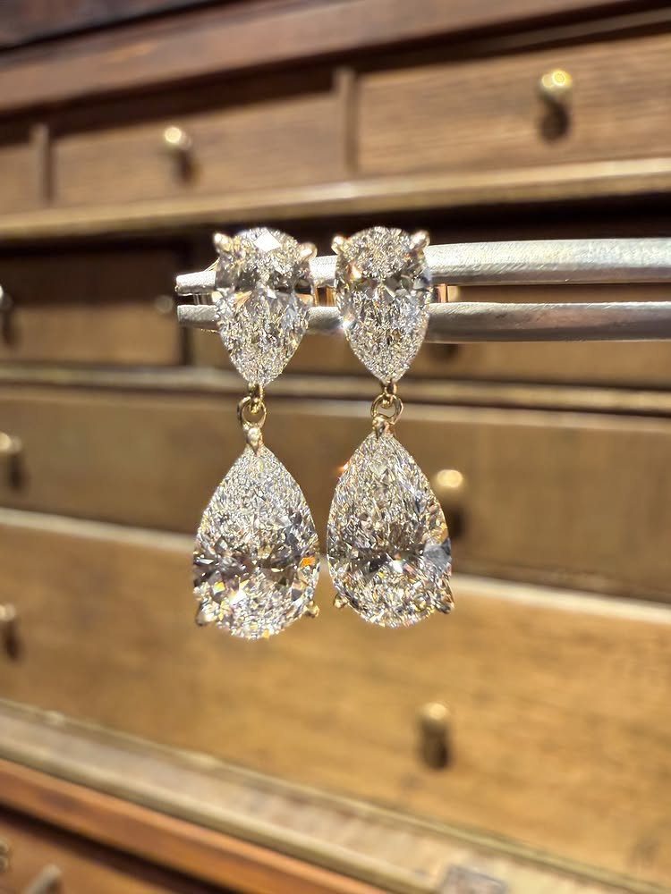 Pair of sparkling pear-shaped vintage diamond drop earrings hanging against a wooden background.