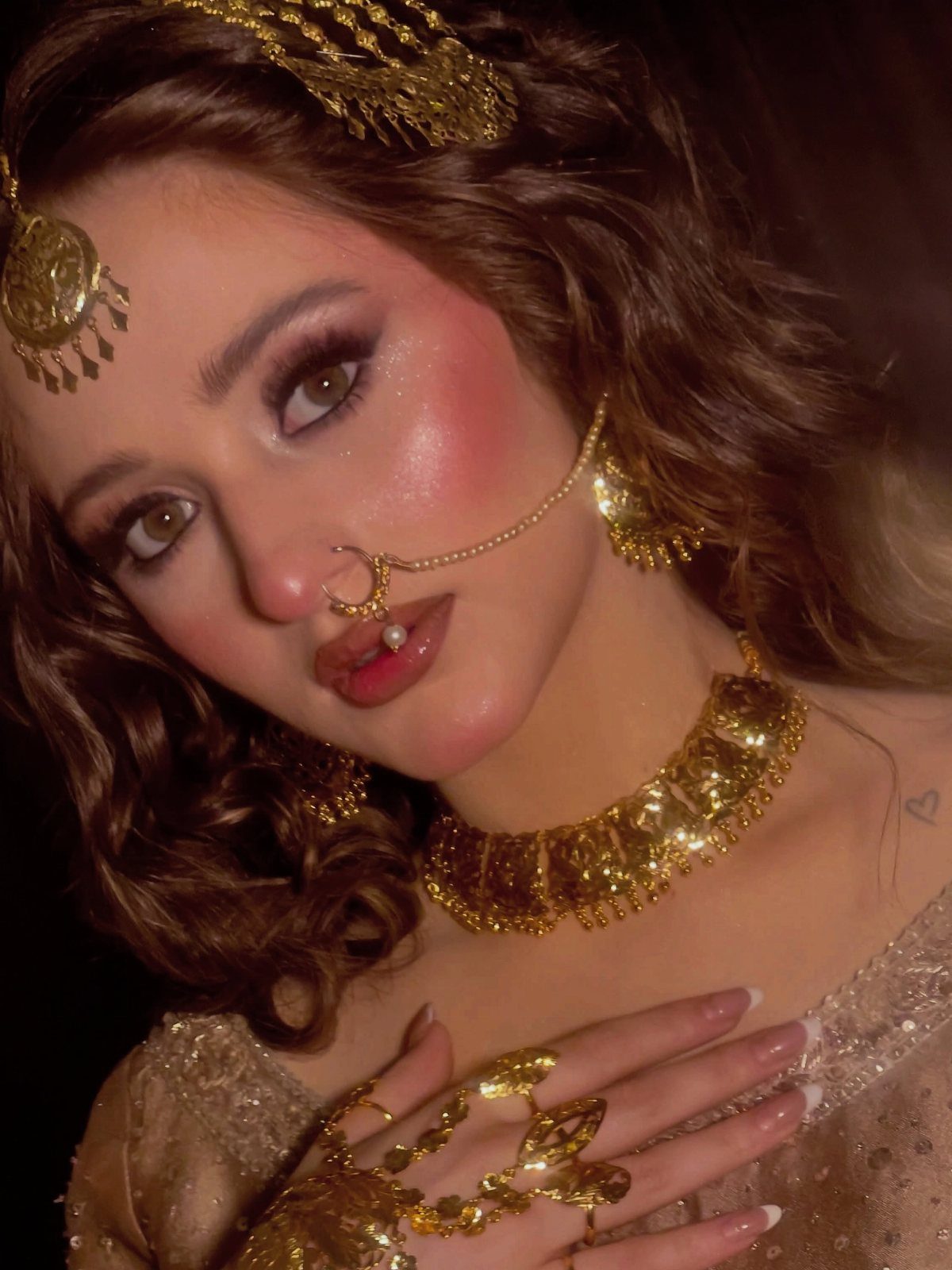 A woman wearing elaborate gold vintage bridal jewelry including a necklace, nose ring, and headpiece.