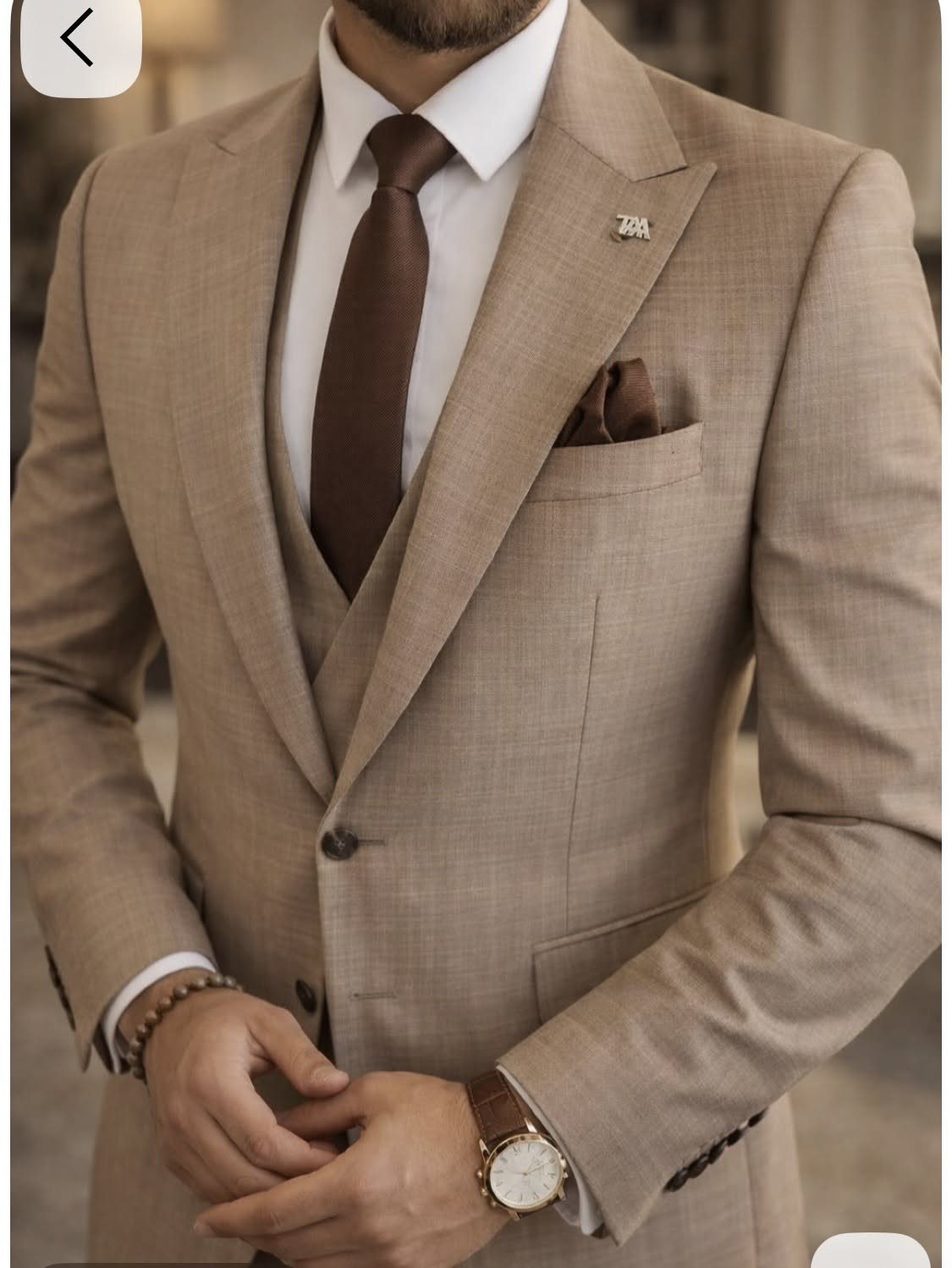 Man wearing a tan textured three-piece suit with a brown tie and pocket square.