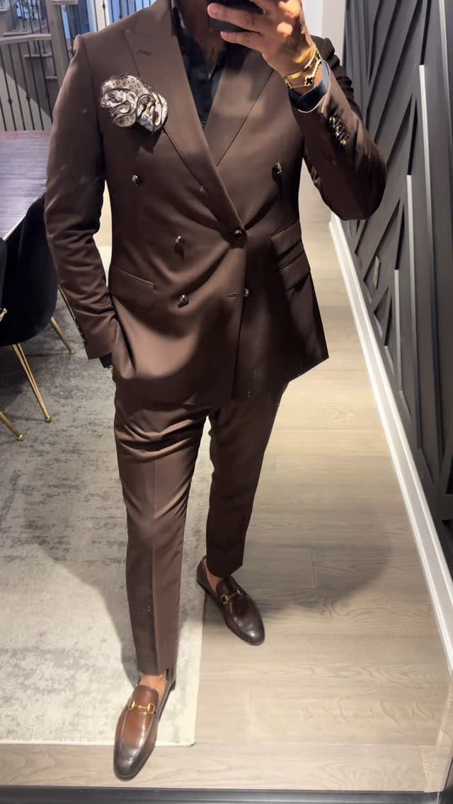 Man in a chocolate brown double-breasted suit and brown loafers taking a mirror selfie.