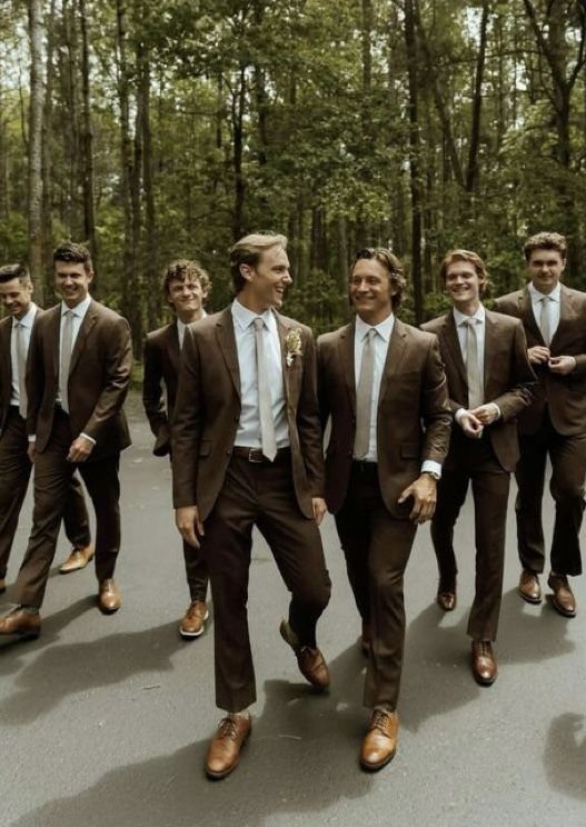 Groomsmen in brown suits and light beige ties walking through a wooded area.