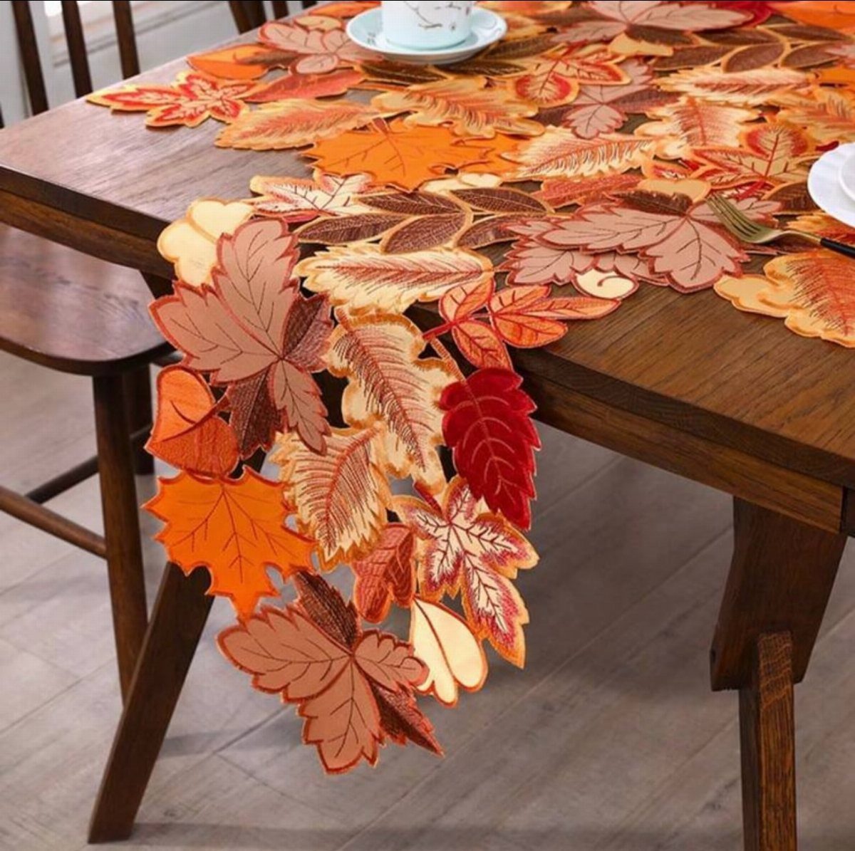 Fabric leaf runner in autumn colors draped over a dark wooden dining table.