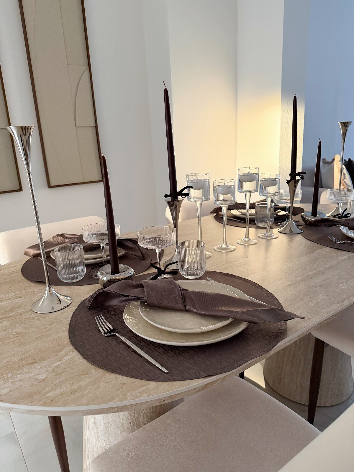 A minimalist dining table set with brown placemats, white plates, and tall black candles.