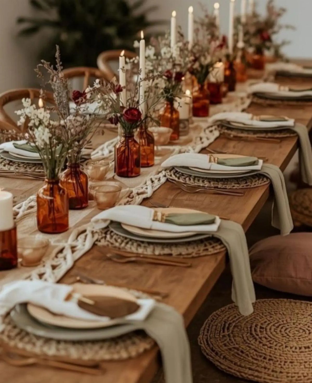 A long wooden table set with amber glassware, white taper candles, and dried floral arrangements.