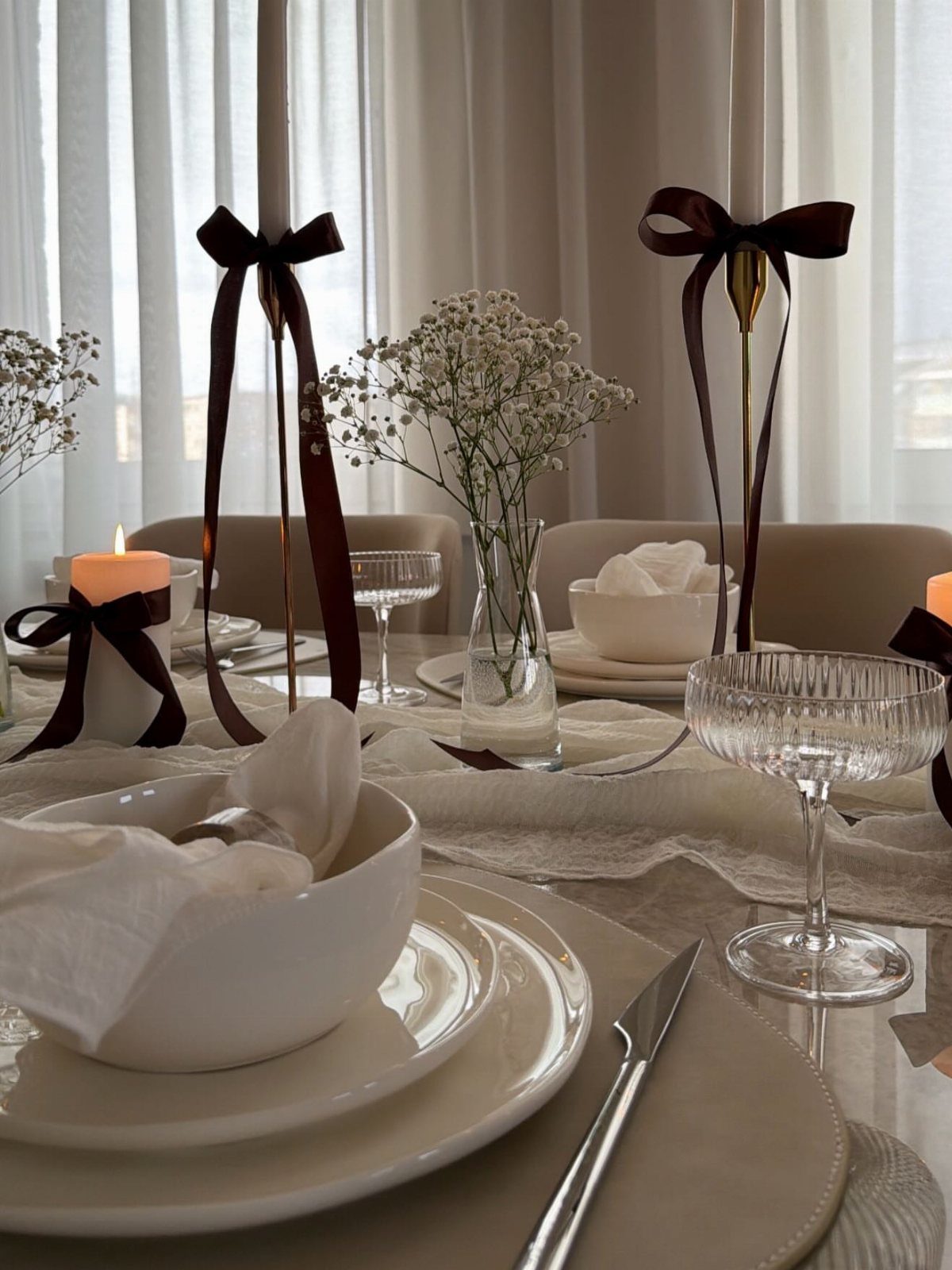 A formal dining table set with white plates, glassware, and dark brown ribbon accents.