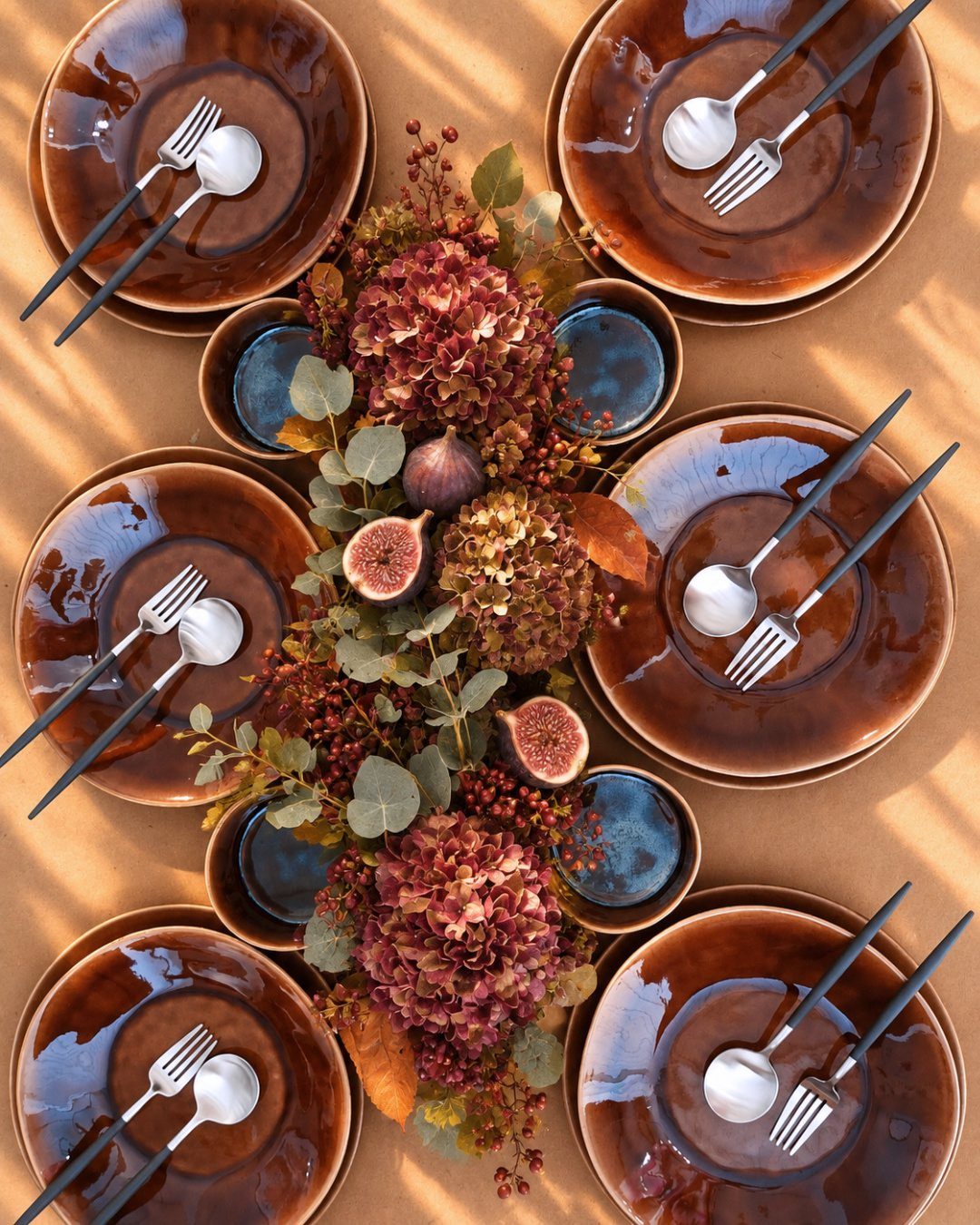 Six hand-painted brown ceramic plates with silver cutlery arranged around a central floral centerpiece.
