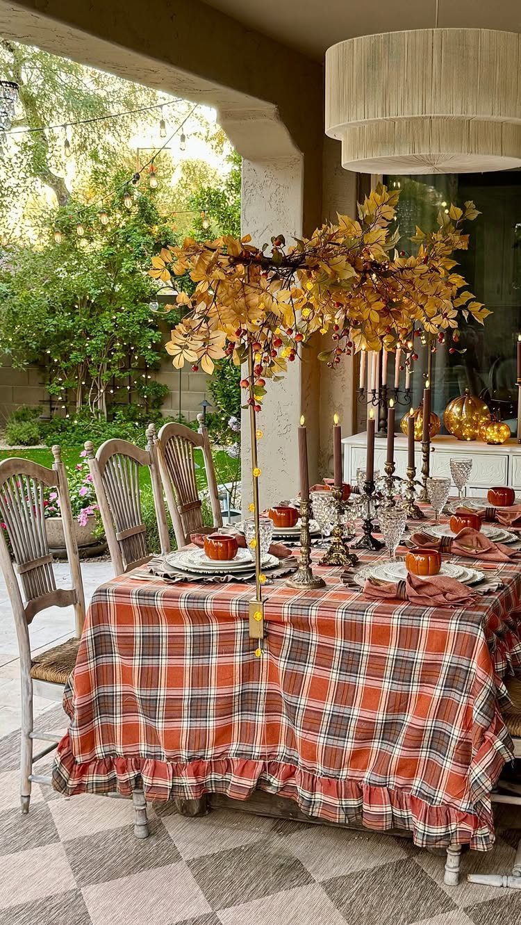 A dining table set with an orange and brown plaid tablecloth and autumn leaf centerpiece.