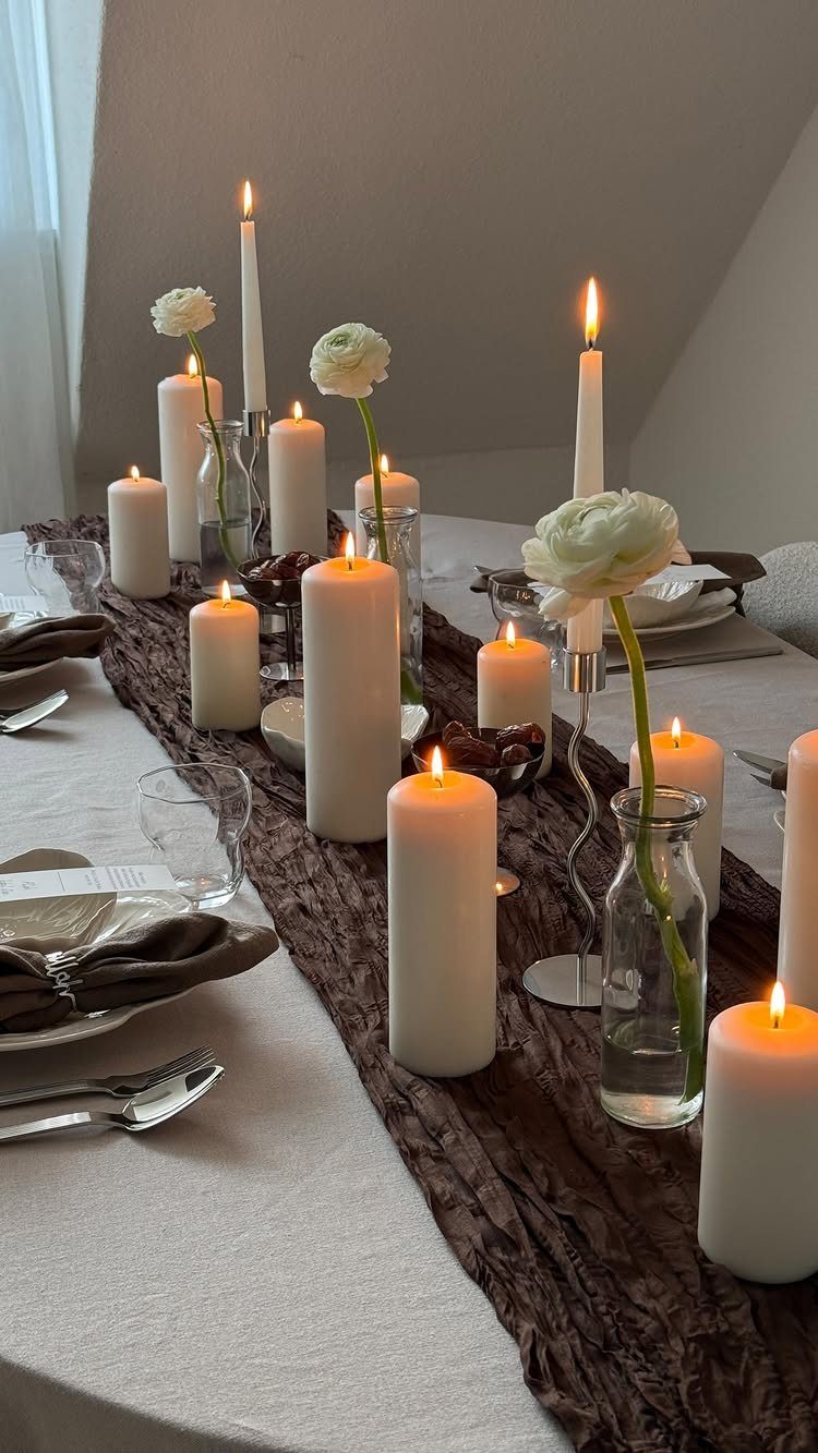 Lit white pillar candles and white flowers arranged on a brown table runner.
