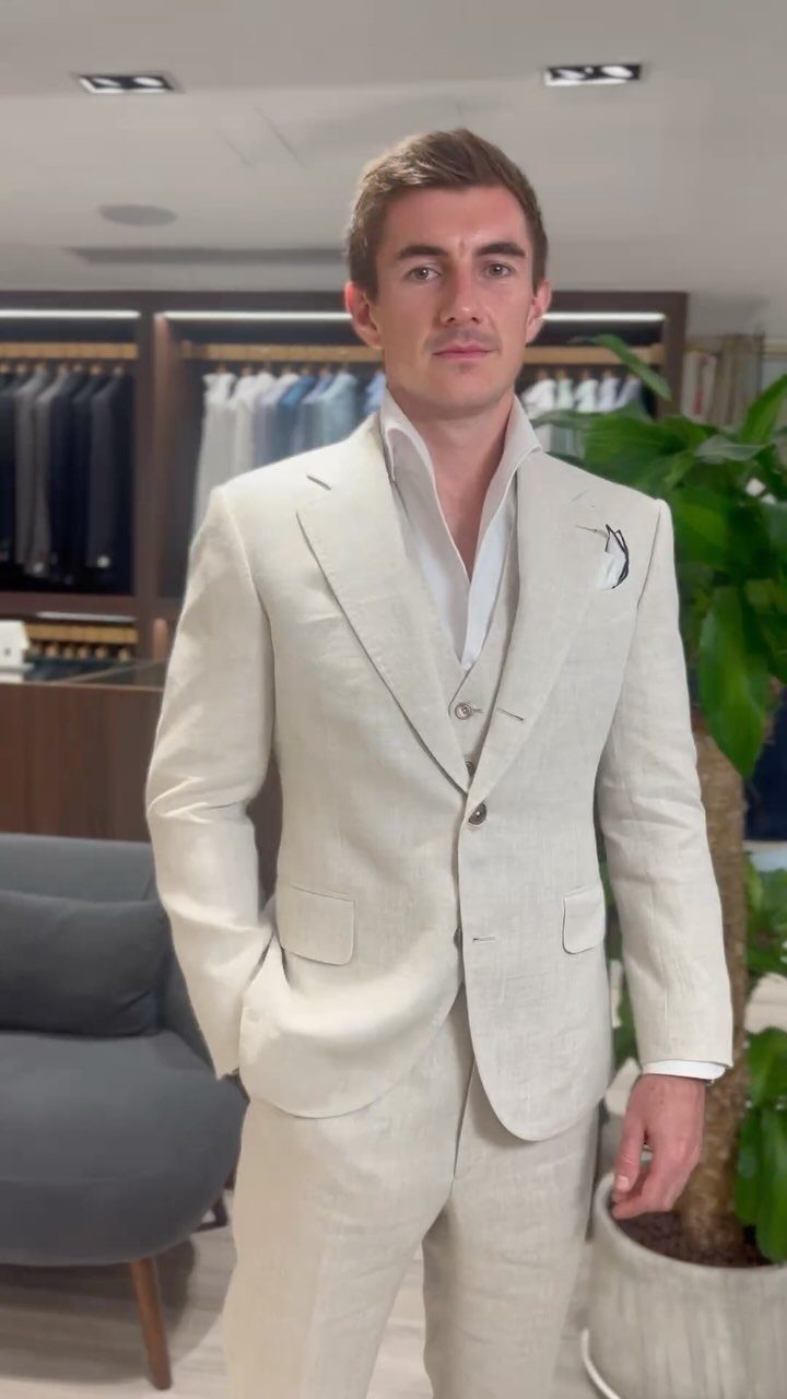 A man posing in a light beige linen three-piece suit and white shirt.