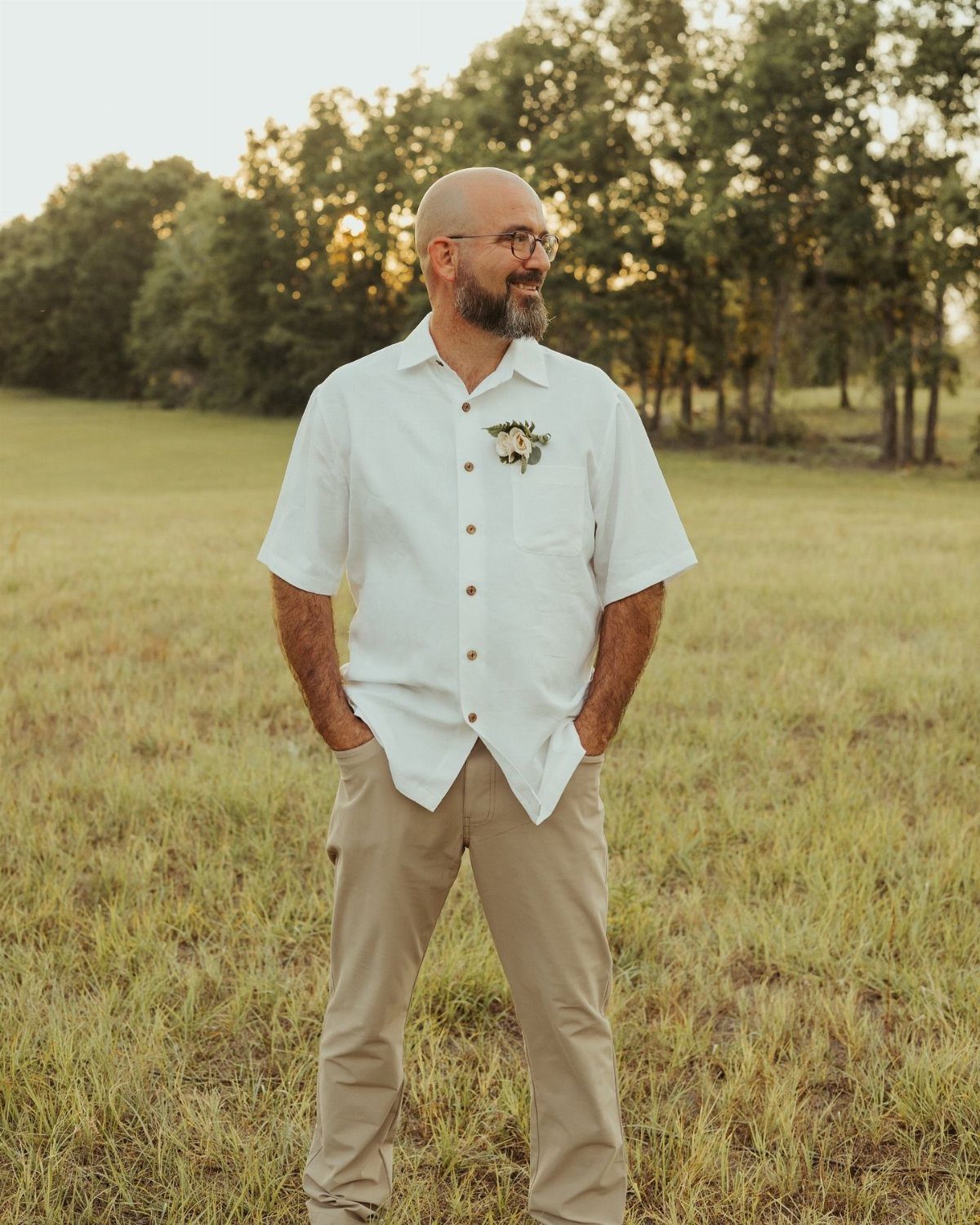 A man wearing a white linen shirt and tan chinos standing in a grassy field.