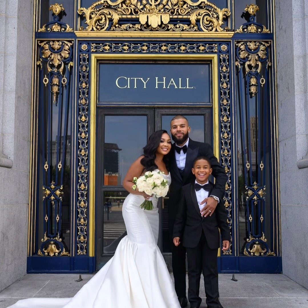 A bride, groom, and young boy posing in front of ornate blue and gold City Hall doors.