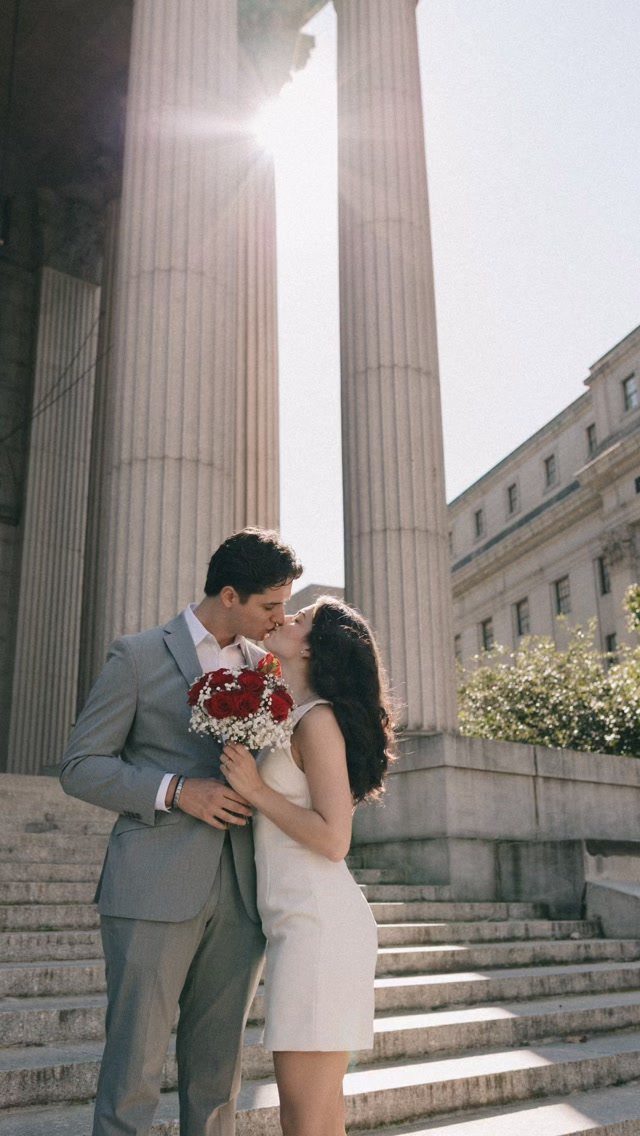 A bride and groom kissing on stone steps in front of large classical columns.