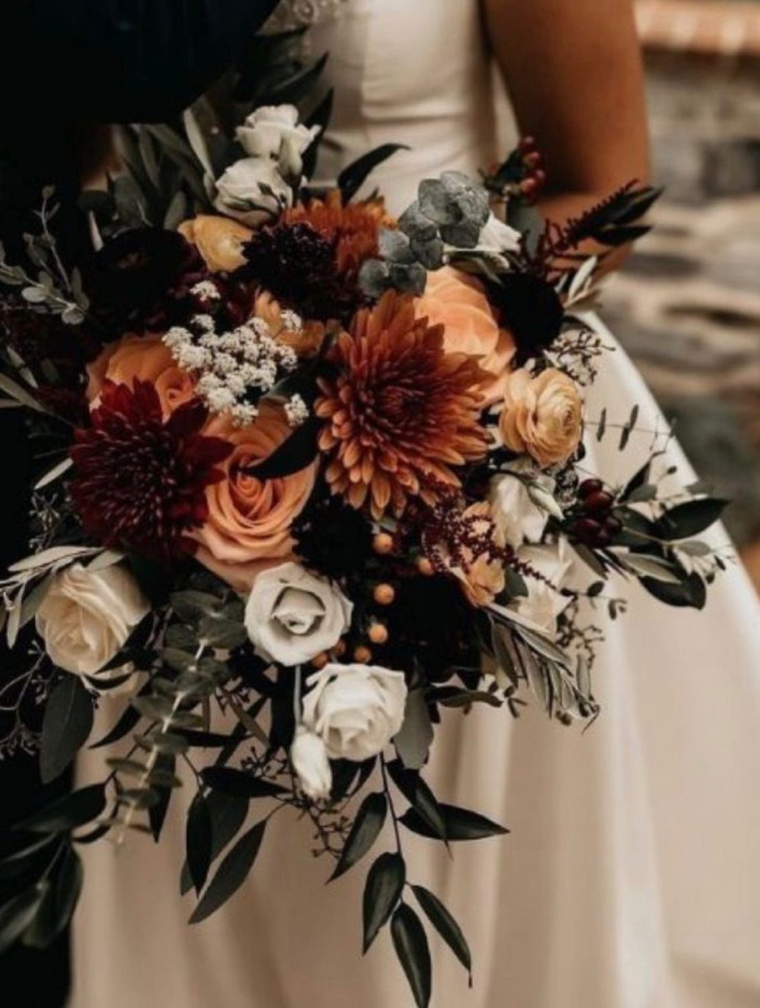 9 Earth Tone Wedding Colors That Feel Grounded, Not Dull 8 A wedding bouquet with terracotta, orange, and cream flowers with dark green leaves.