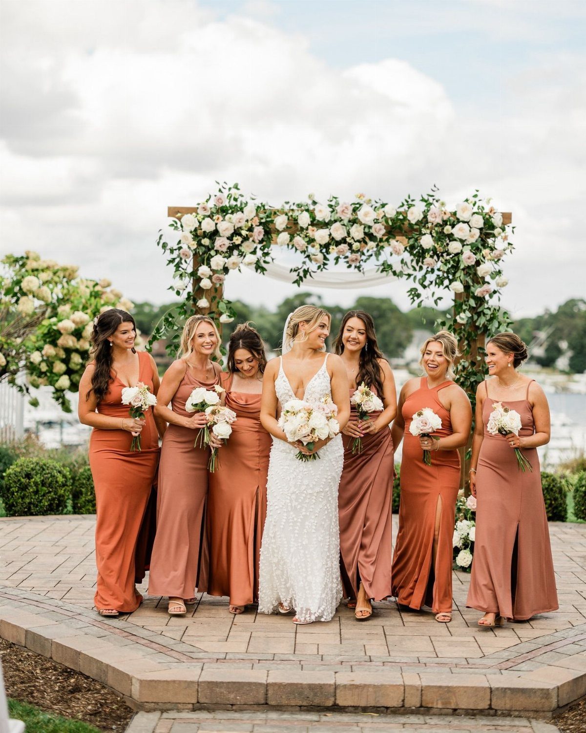 9 Earth Tone Wedding Colors That Feel Grounded, Not Dull 2 Bridesmaids in terracotta and dusty rose dresses standing with a bride in white lace.