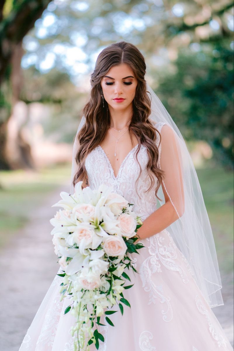 A bride with long wavy hair and a sheer tulle veil holding a white lily bouquet.