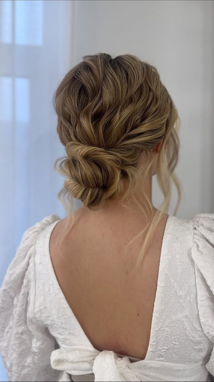 Blonde hair styled in a loose wavy low bun on a woman wearing a white dress.