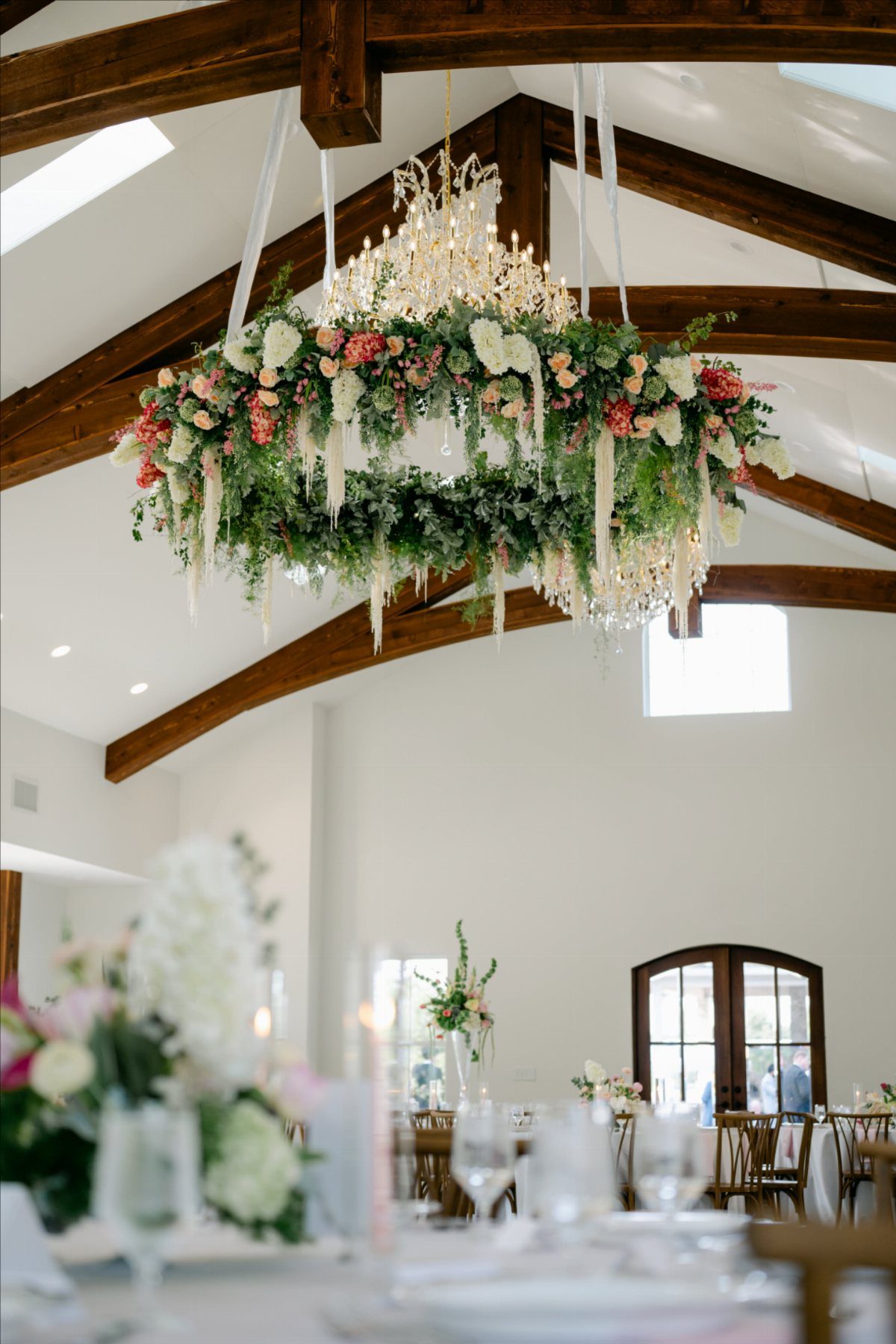 A crystal chandelier decorated with a thick ring of pink and white flowers and greenery.