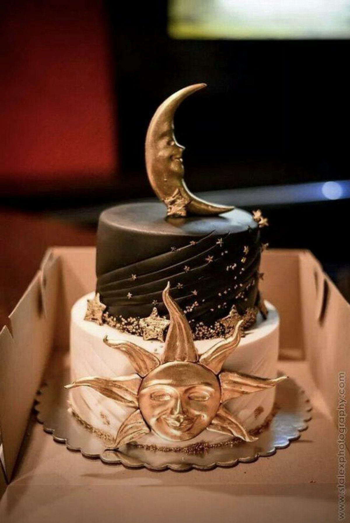 Two-tier celestial cake with a gold sun on the bottom and a gold crescent moon topper.