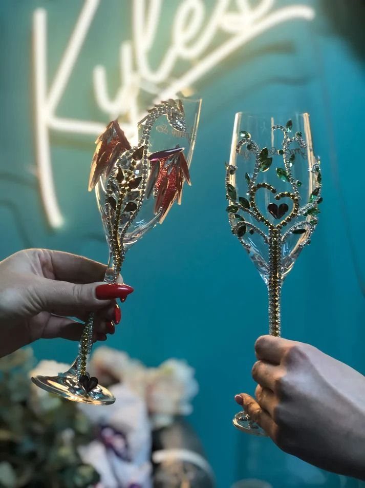 Two ornate fantasy-themed champagne flutes held up against a dark teal background.