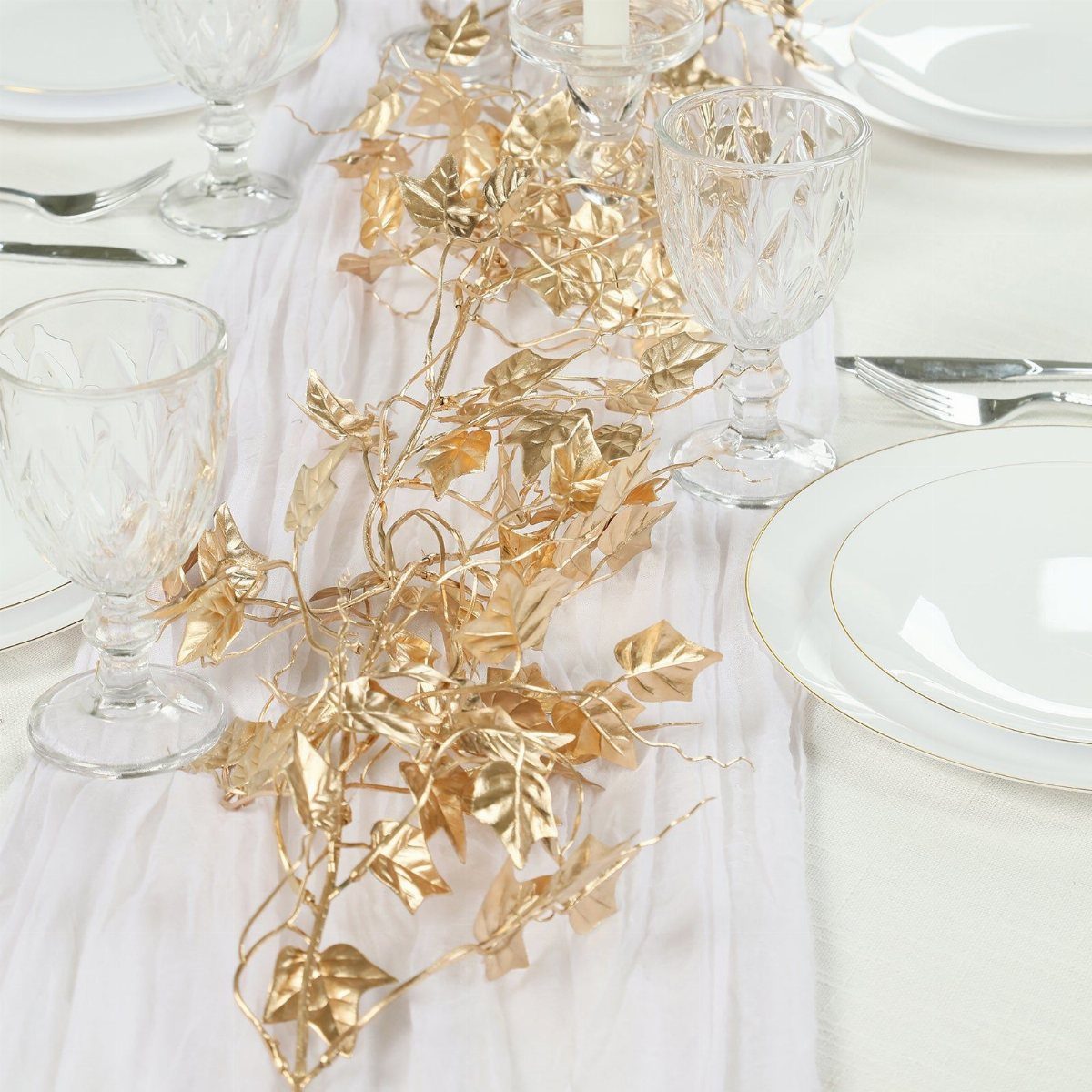 Gold metallic leaf garlands draped over a white fabric runner on a formal dining table.