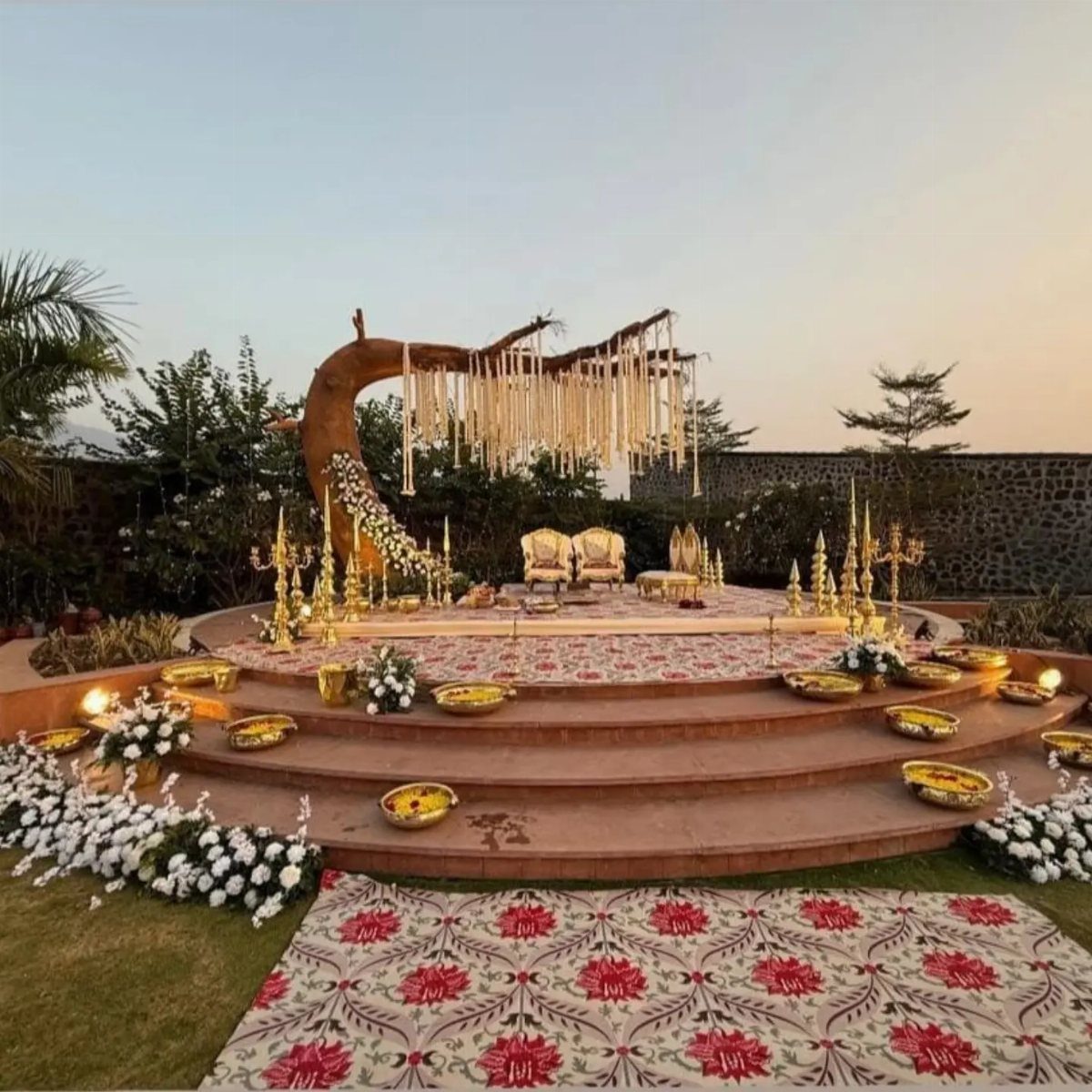 Twisting tree branch arch with hanging white flowers over a decorated outdoor wedding stage.