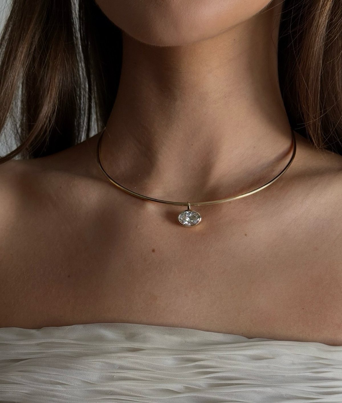 A gold-toned metal choker necklace with a single round gemstone pendant worn on a person's neck.