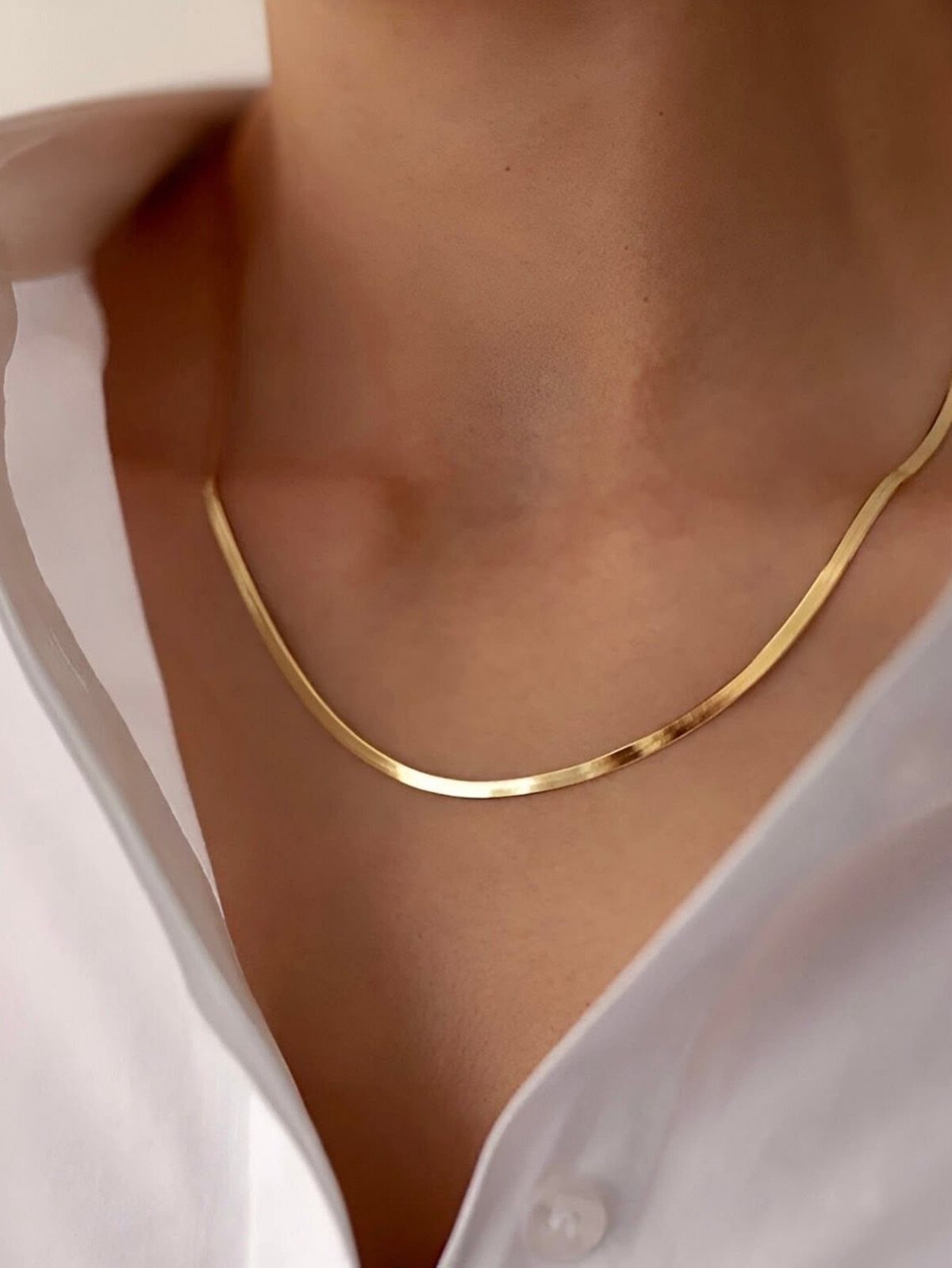 A gold snake chain necklace worn around a person's neck over a white shirt.