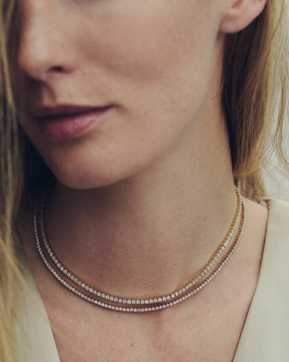 A woman wearing two delicate gold-toned tennis style necklaces with small sparkling stones.