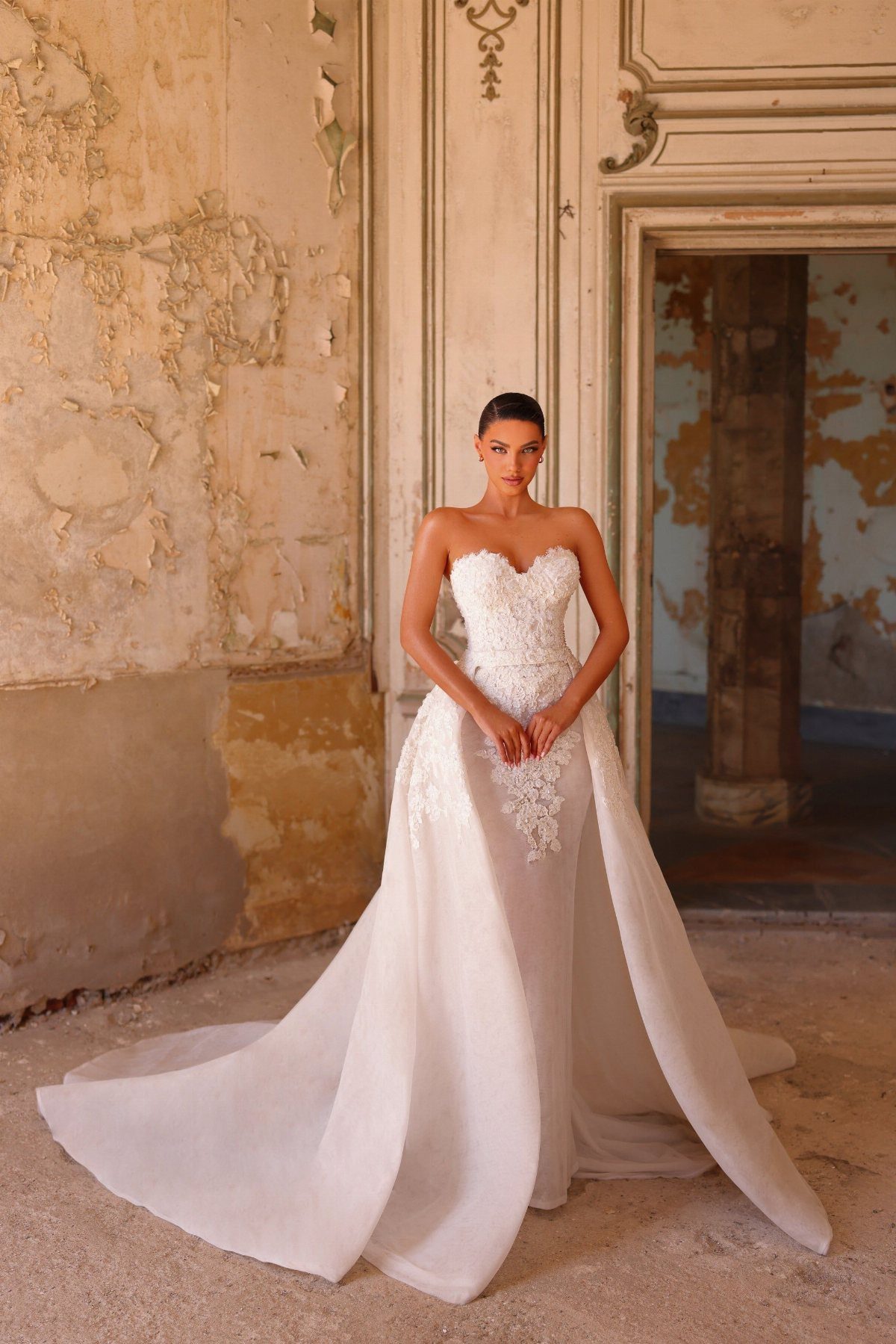 Woman wearing a white lace wedding gown with a large, voluminous detachable overskirt.