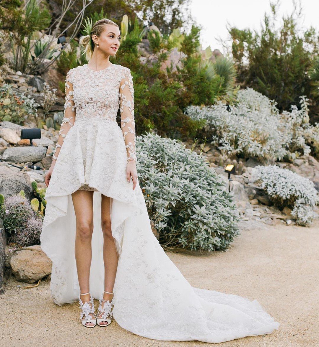 Woman in a white lace wedding gown with a high-low hemline standing in a desert garden.