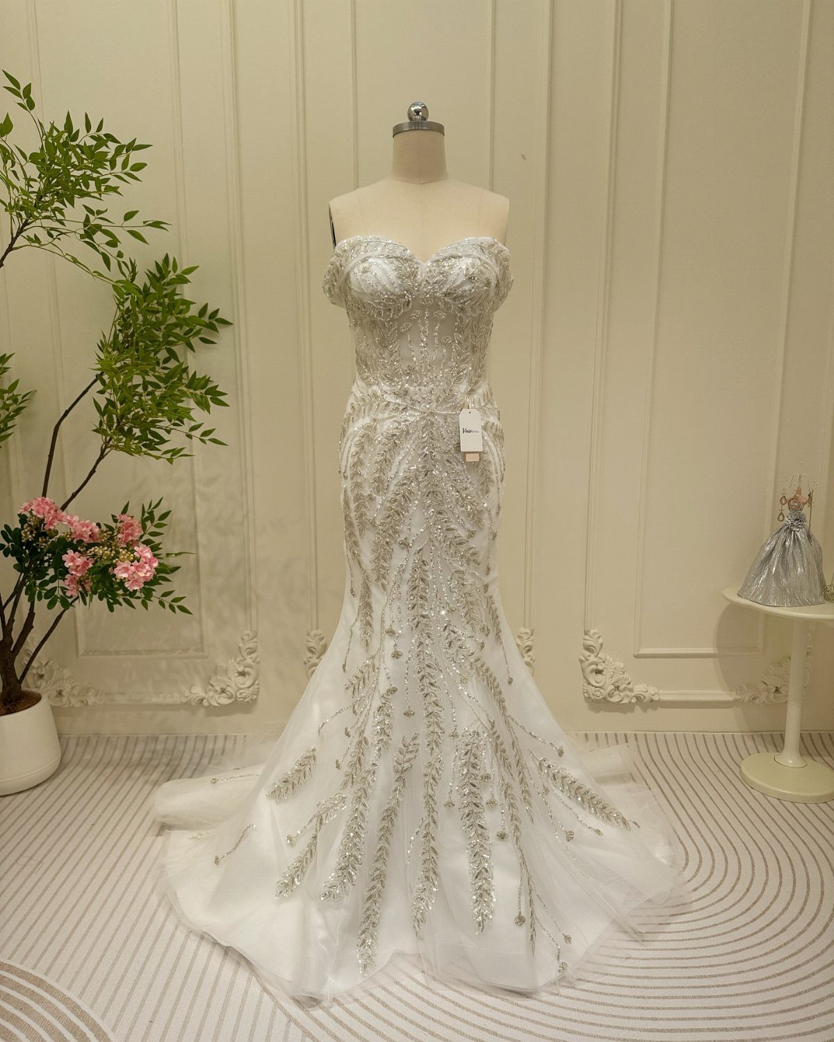 A white mermaid wedding gown with silver crystal embellishments displayed on a mannequin.