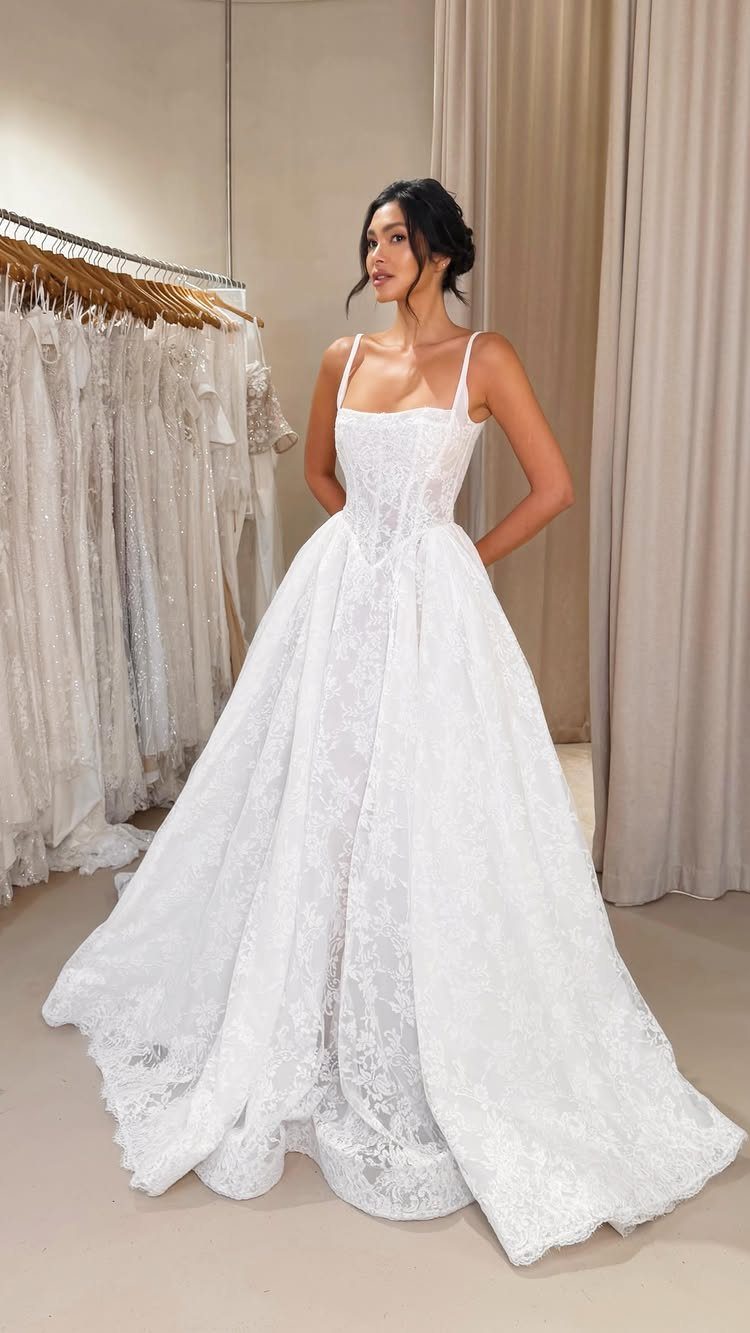 Woman wearing a white lace wedding gown with a fitted, structured bodice and voluminous skirt.