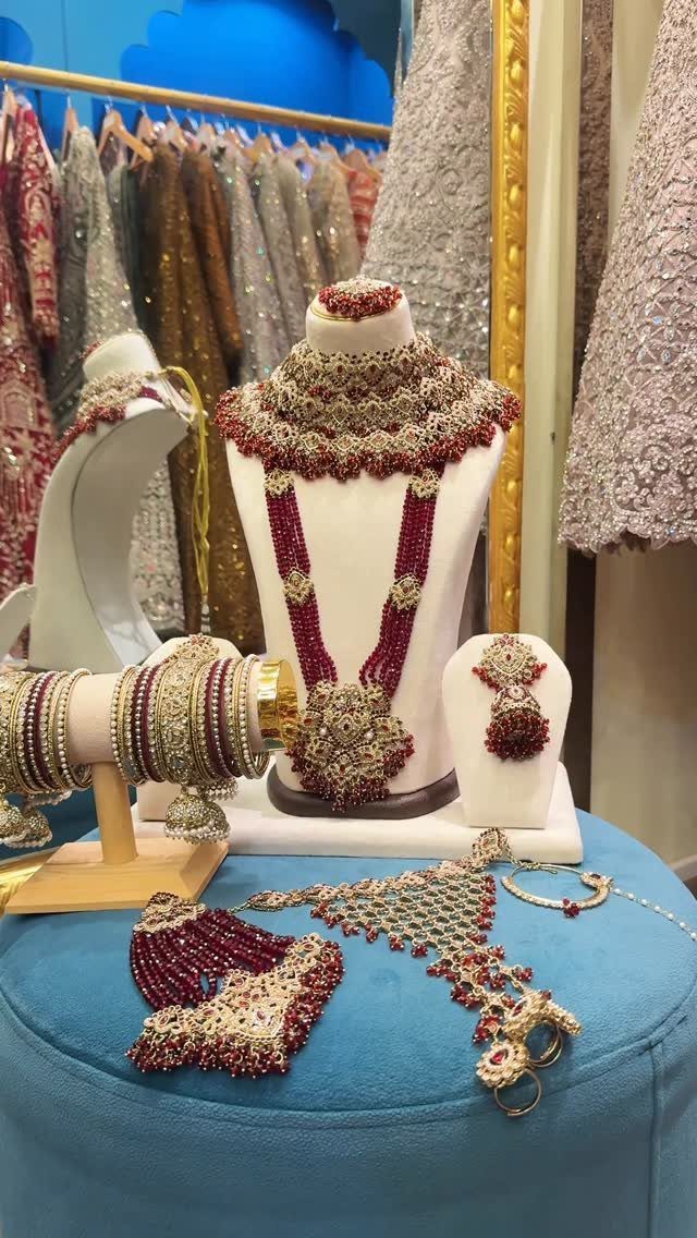 Ornate gold and ruby-colored jewelry displayed on white busts and a blue velvet surface.